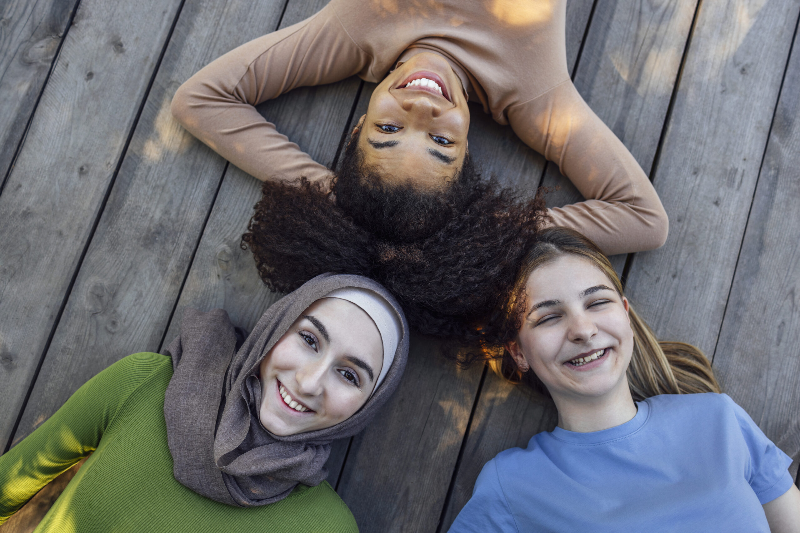 Multiracial young teen female friends resting in the park after sport training laughing and having fun together. Diversity, sport and friendship concept